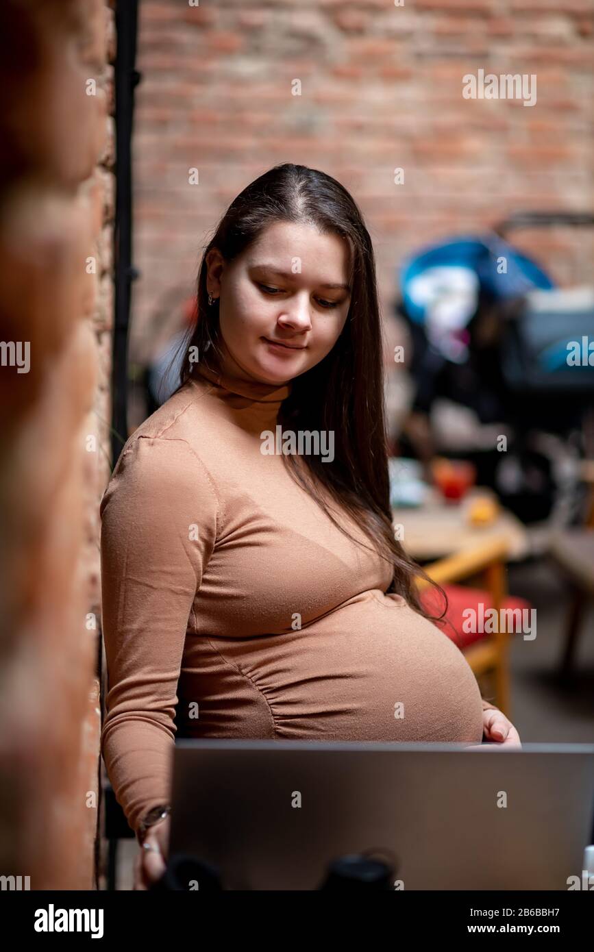 Portrait de jeune femme indépendante prégnanty utilisant un ordinateur portable pour un travail à distance tout en étant assis dans un café moderne avec une tasse de thé Banque D'Images