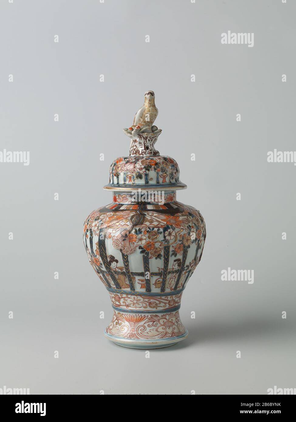 Vase balustre avec couverture pour les personnes dans une calandre intérieure arrière, prunus arbres et les tendons de fleurs Balustervormigue dekselpot van porselein met een spireidande voet, beschilderd dans onderglacuur blauw en op het glasuur rood, zwart en goud. Op de wand twee keer twee mensen zittend in een interieur achter gemodelleerd en beschilderd traliewerk. Dit traliewerk est versierd met gemodelleerde en gedecoreerde prunusbomen en banden met bloemranken. Onder het traliewerk een band met bloemranken. Rond de voet een groupe a rencontré lotusranken. Op de hals drie cartridges met lotusranken. Imari. Fabricant : pottenbak Banque D'Images