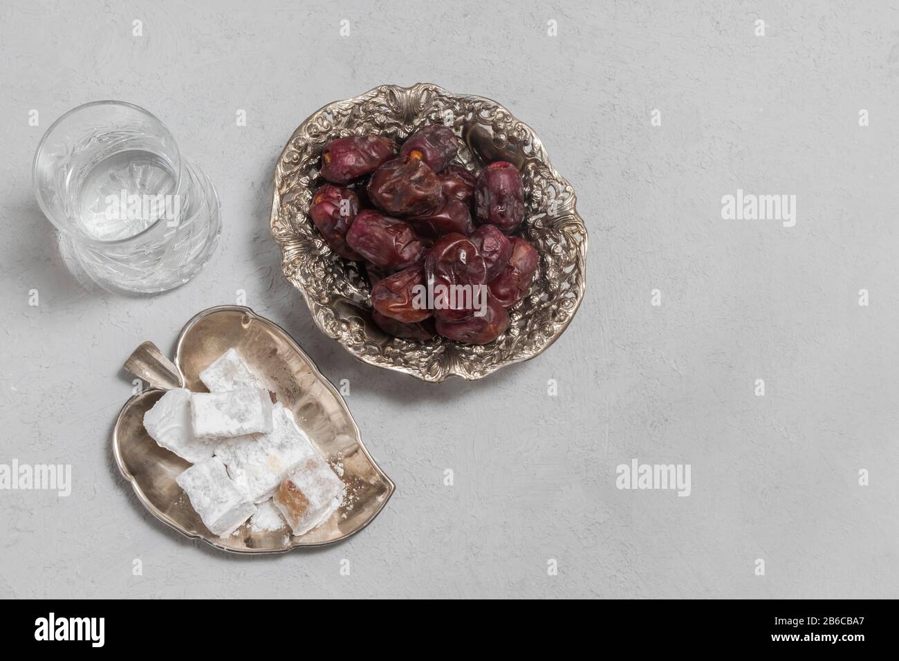 Vue de dessus de la nourriture douce pour Ramadan (lokum et dattes sèches) avec verre d'eau sur fond de béton neutre avec espace de copie Banque D'Images