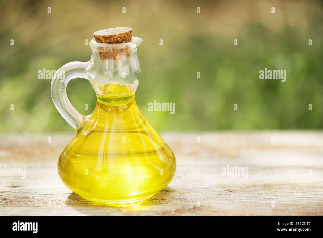 Bouteille de verre pleine d'huile végétale dorée sur une table en bois sur un fond vert flou. Maquette pour huile de salade ou graisse végétale Banque D'Images