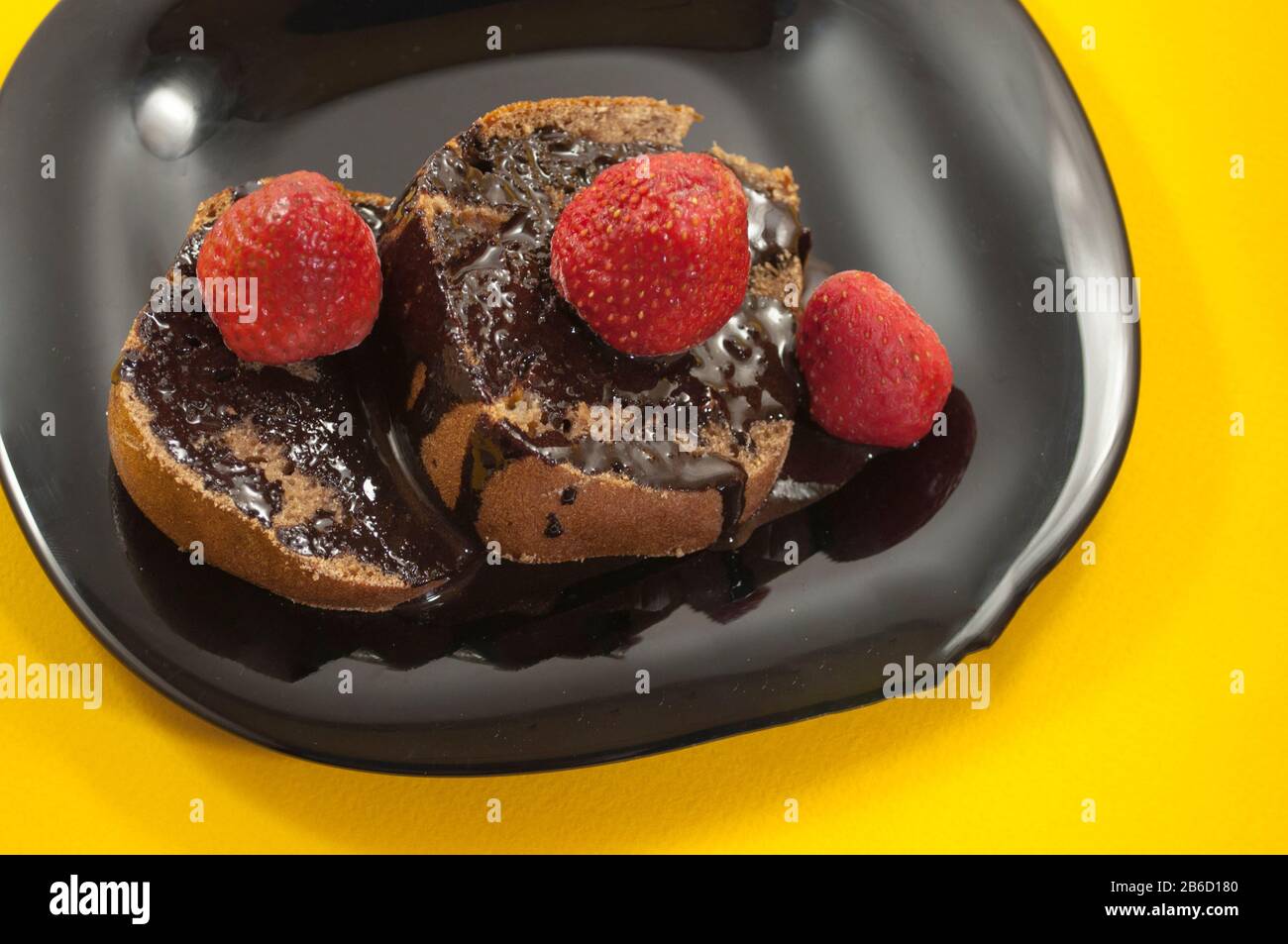 représentant deux morceaux de gâteau enrobé de chocolat avec plusieurs fraises sur le dessus en plaque noire sur fond de table jaune Banque D'Images