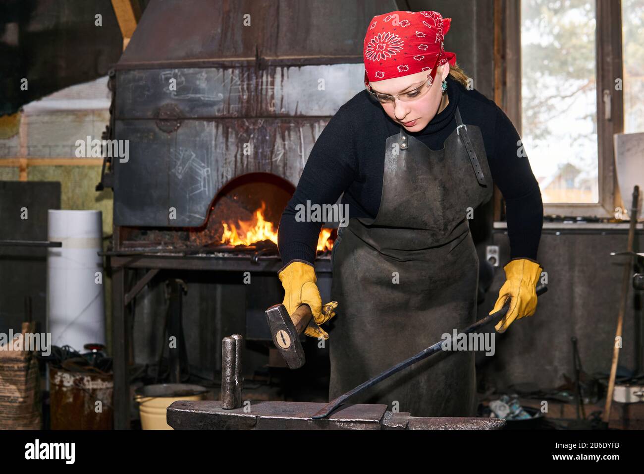 femme forgeron métal artiste forge une pièce de métal chaude avec marteau sur l'enclume dans un atelier traditionnel Banque D'Images