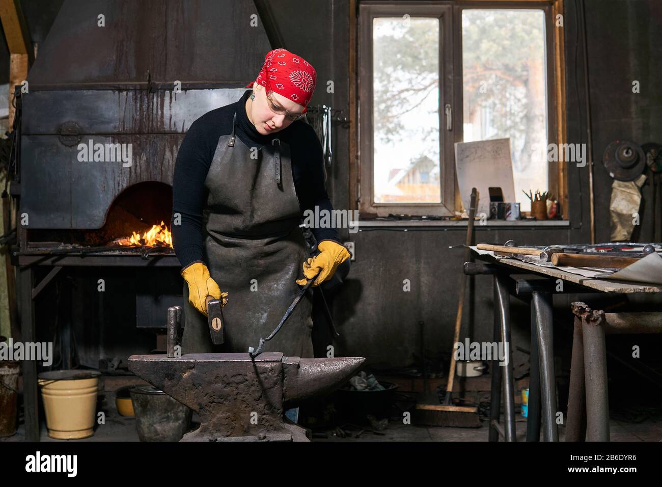 femme forgeron métal artiste forge un blanc de métal figuré avec marteau sur l'enclume dans un atelier traditionnel Banque D'Images