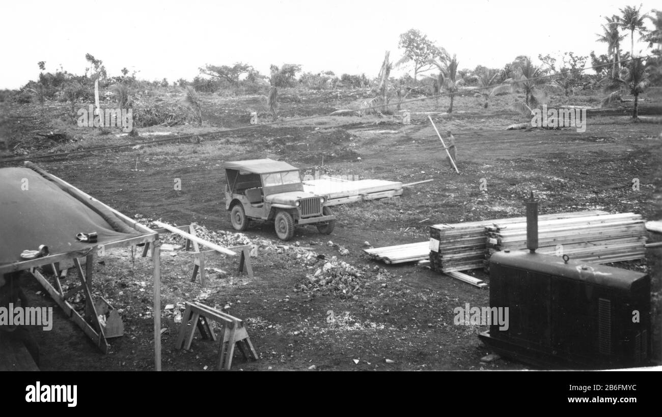 Seabees sur Guam, n° 2, 16 novembre 1944. Un homme dans le Lean-to et un autre bois de charpente de transport sont en train de mettre en place la zone d'assemblage pour les bâtiments à venir. Voir la boîte à outils, le cheval de scie, les piles de bois d'œuvre, et un générateur de taille Jeep en bas à droite. Ma photo suivante montre une route de gravier devant les arbres cassés derrière la jeep. Cette photo montre également deux zones de terrain qui ont été classées pour les bâtiments à venir. Ces Seabees commencent à construire des routes et des bâtiments pour les bâtiments des officiers du CINCPAC. Pour voir mes images vintage connexes, recherchez: Prestor vintage WW II véhicule Banque D'Images