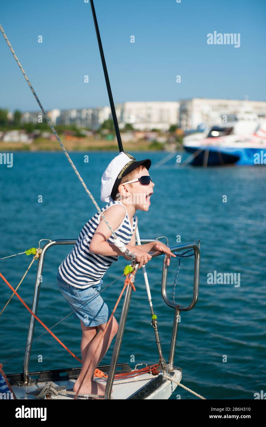 charmant petit enfant drôle dans un chapeau blanc capitaine et des lunettes  de soleil riant sur le bateau à voile de mer pendant les vacances d'été  voyage dans le port de l'océan