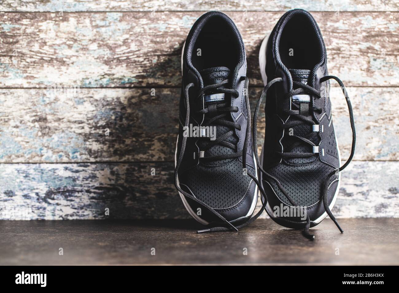 Chaussures de sport noires avant l'ancien mur en bois. Banque D'Images
