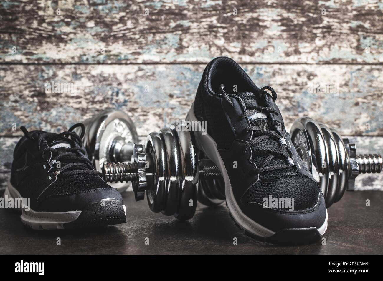 Concept de forme physique. Chaussures de sport noires et haltères avant le vieux mur en bois. Banque D'Images