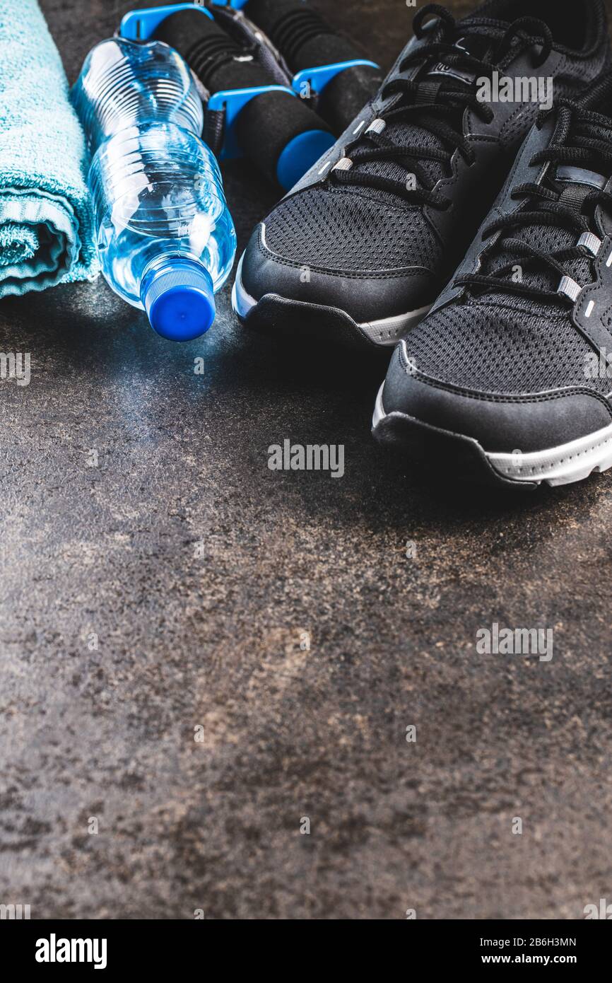 Concept de forme physique. Chaussures de sport noires, serviette, haltères et bouteille d'eau sur la vieille table. Banque D'Images