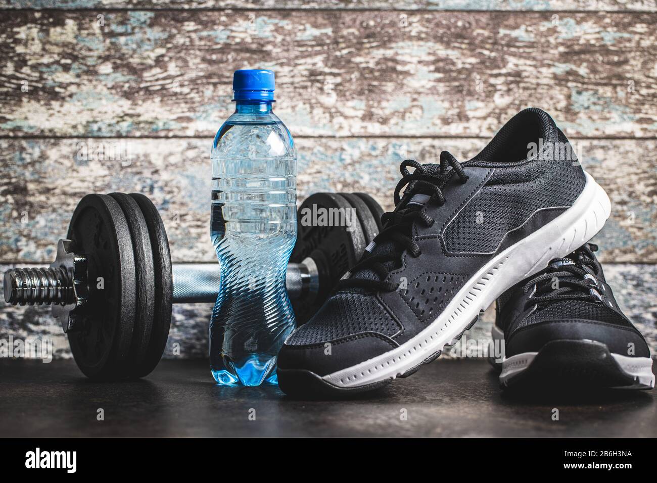 Concept de forme physique. Chaussures de sport noires, haltère et bouteille d'eau avant le vieux mur en bois. Banque D'Images
