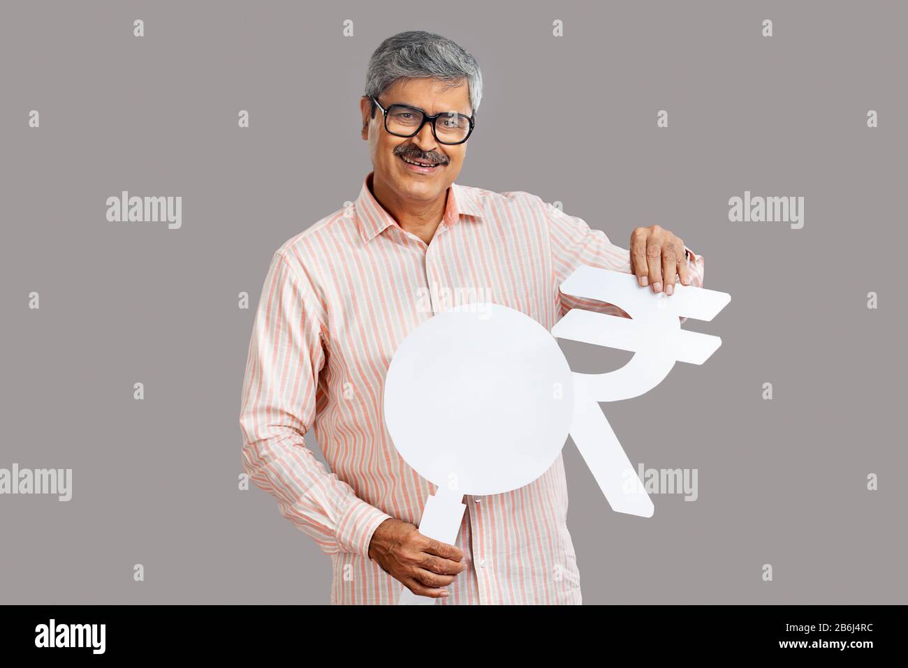 Homme senior portant un symbole de roupie et une loupe en carton. Banque D'Images