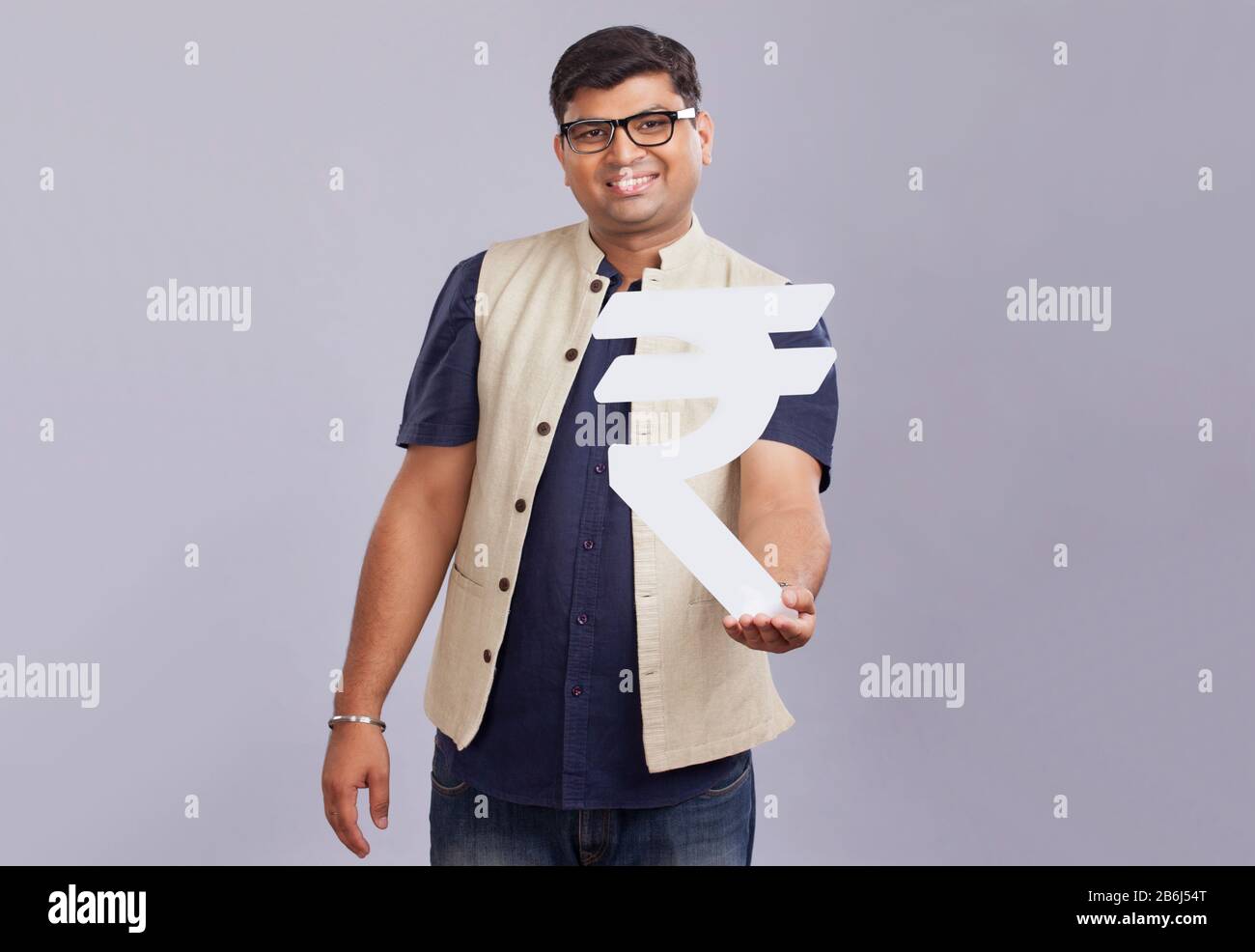 Homme tenant un symbole de roupie fait de carton. Banque D'Images