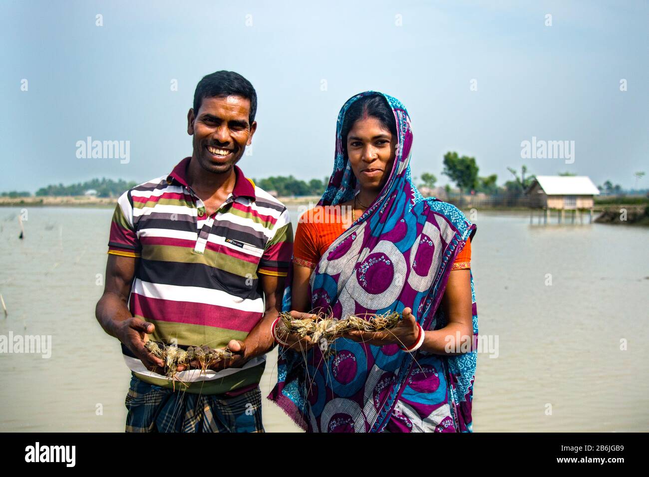 Un homme et une femme tiennent le poisson dans leur main et le visage heureux car ils sont heureux avec le poisson et les crevettes qu'ils ont récoltées de leur étang. Banque D'Images