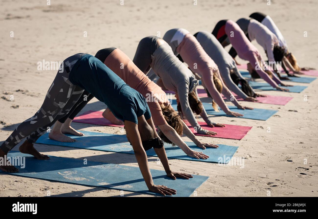 Vue latérale des femmes qui font des positions de yoga à la plage Banque D'Images