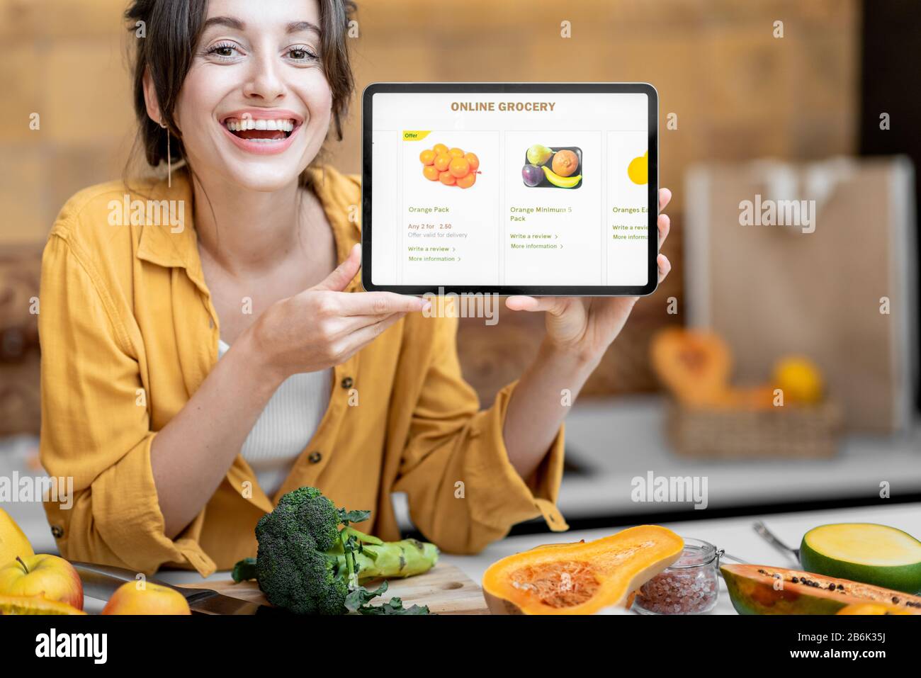 Femme tenant une tablette numérique avec le marché de shopping en ligne lancé tout en se tenant sur la cuisine avec beaucoup de nourriture fraîche sur la table Banque D'Images