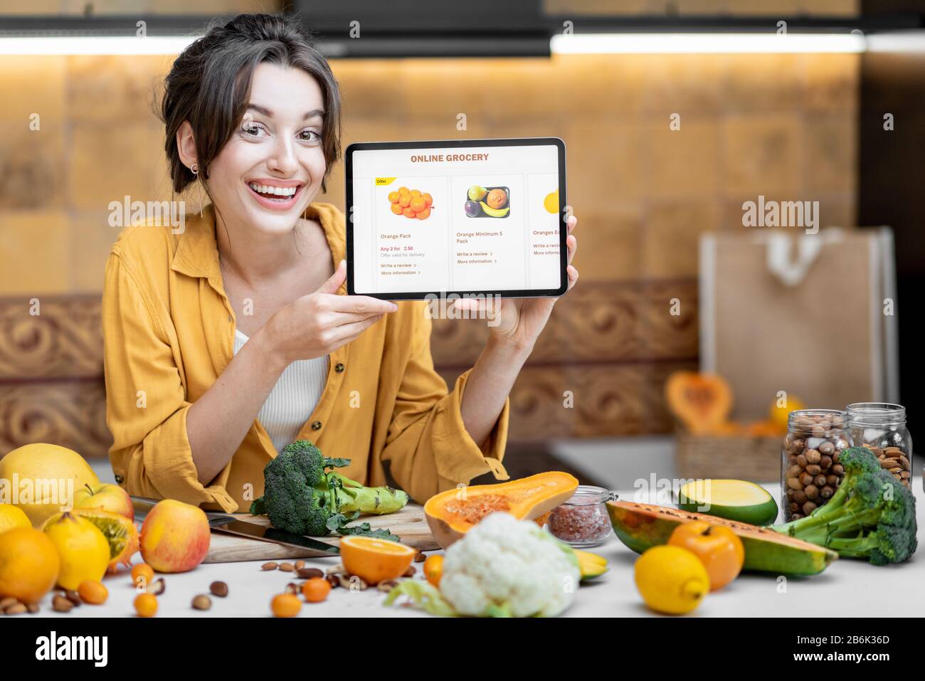 Femme tenant une tablette numérique avec le marché de shopping en ligne lancé tout en se tenant sur la cuisine avec beaucoup de nourriture fraîche sur la table Banque D'Images