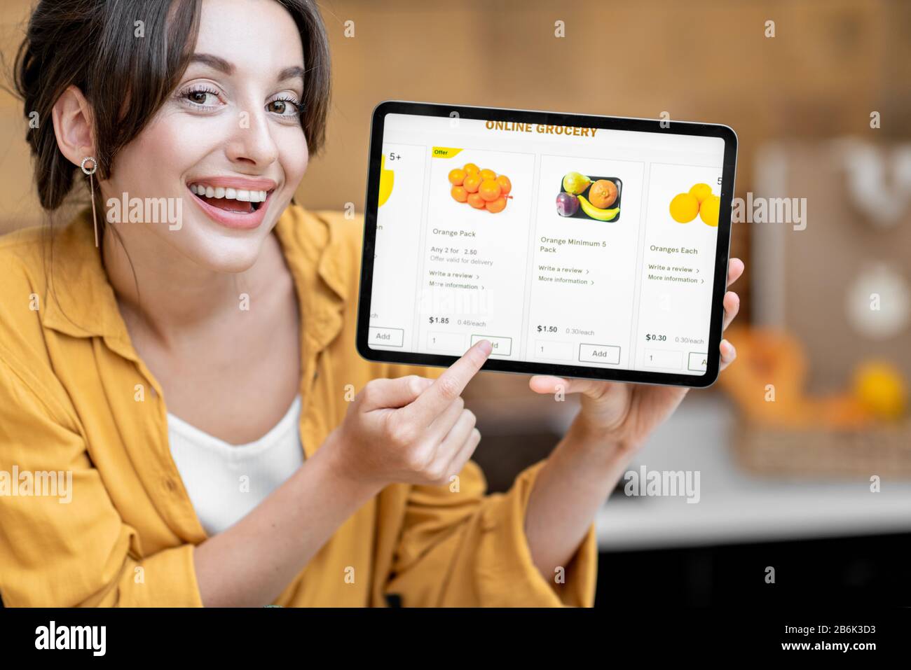 Femme tenant une tablette numérique avec le marché de shopping en ligne lancé tout en se tenant sur la cuisine avec beaucoup de nourriture fraîche sur la table Banque D'Images