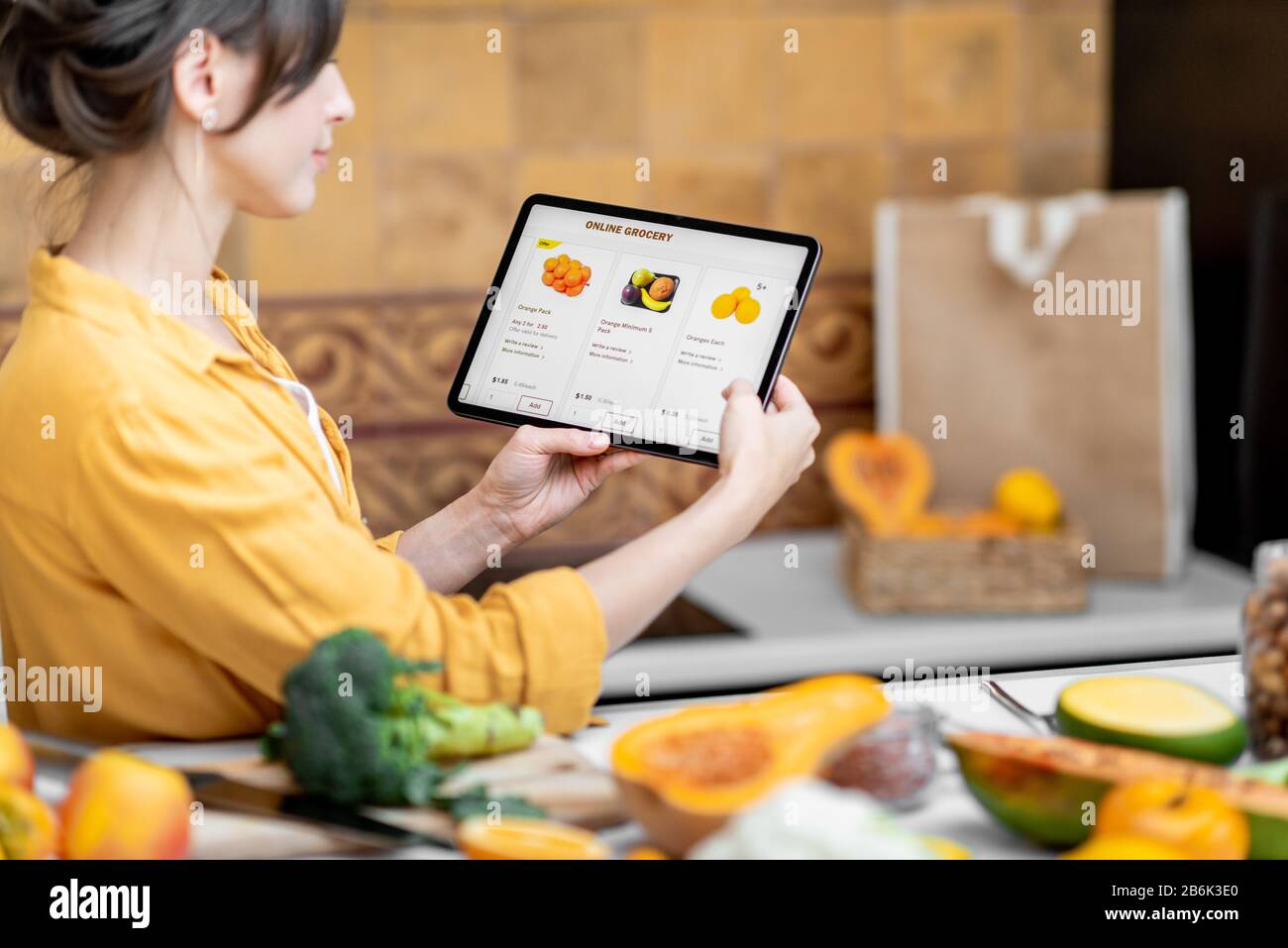 Femme tenant une tablette numérique avec le marché de shopping en ligne lancé tout en se tenant sur la cuisine avec beaucoup de nourriture fraîche sur la table Banque D'Images