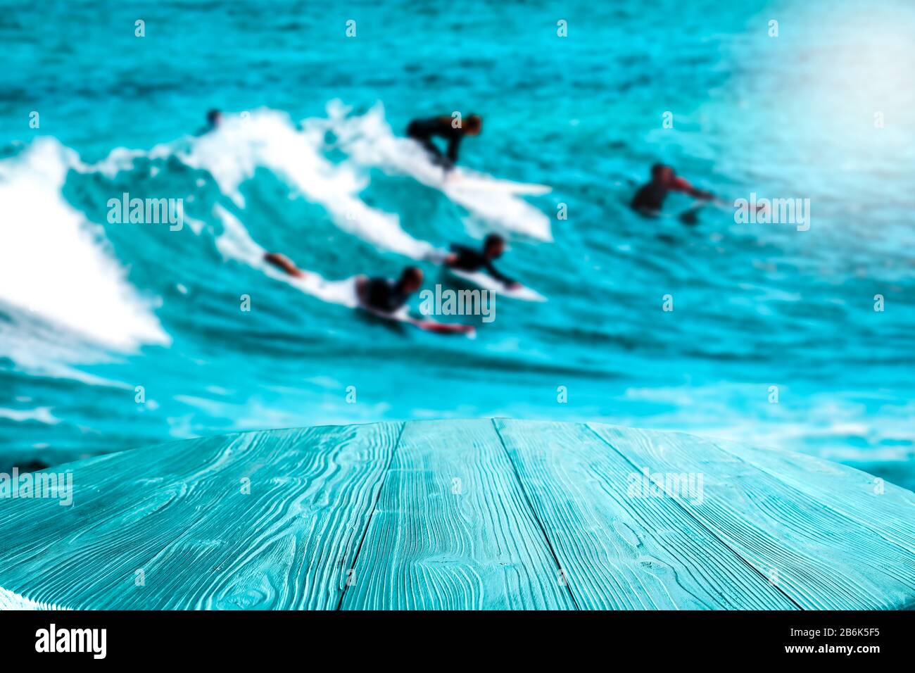 Surfeurs sur les vagues dans l'océan turquoise. Table en bois bleu avec espace pour votre décoration et vos produits publicitaires. Joyeux été ensoleillé Banque D'Images