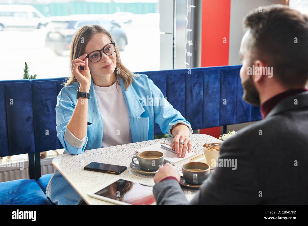 Jeune femme d'affaires séduisante qui ajuste les lunettes et discute avec un collègue lors d'une réunion dans un café moderne Banque D'Images