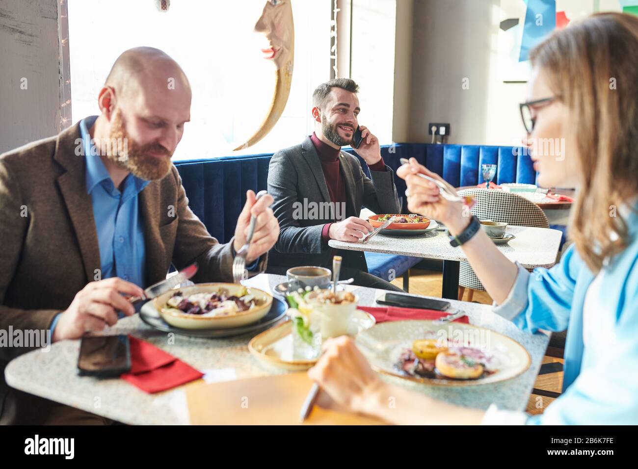 Les gens d'affaires dans le café : un jeune homme d'affaires réussi à manger de la salade et à discuter des affaires par téléphone pendant que les collègues ont déjeuner ensemble Banque D'Images