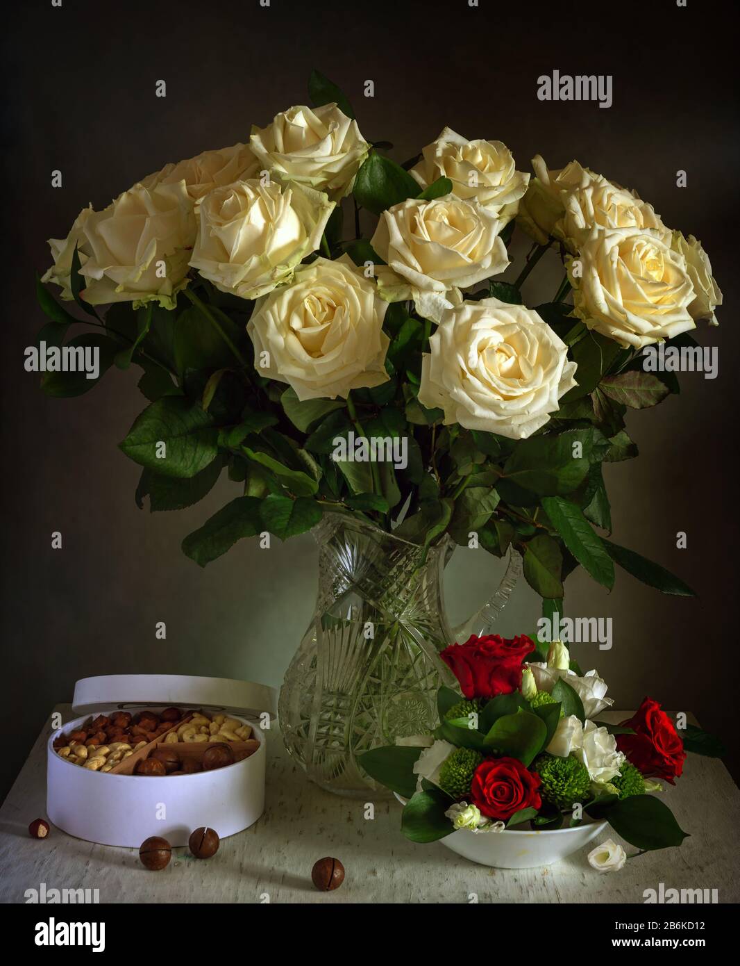 Un beau bouquet de roses dans une verseuse en cristal et une boîte aux fruits à coque savoureux. Toujours la vie. Vintage. Banque D'Images