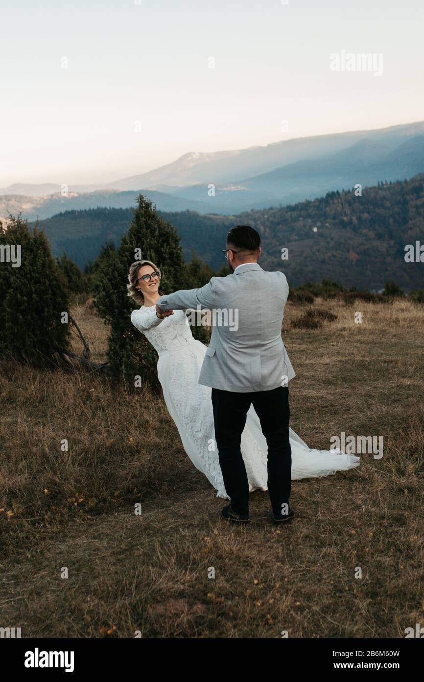 Beau couple ayant un moment romantique sur leur journée de désherbage, dans les montagnes au coucher du soleil. Jouer ensemble. La mariée est dans une robe de mariage blanche. Banque D'Images