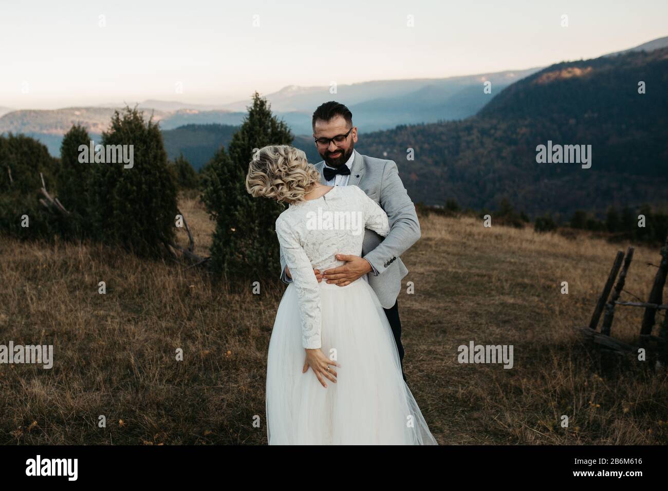 Beau couple ayant un moment romantique sur leur journée de désherbage, dans les montagnes au coucher du soleil. Jouer ensemble. La mariée est dans une robe de mariage blanche. Banque D'Images