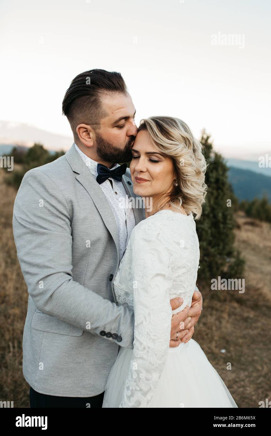 Beau couple ayant un moment romantique sur leur journée de désherbage, dans les montagnes au coucher du soleil. Mariée dans une robe de mariage blanche. Heureux couple embrassant. Banque D'Images