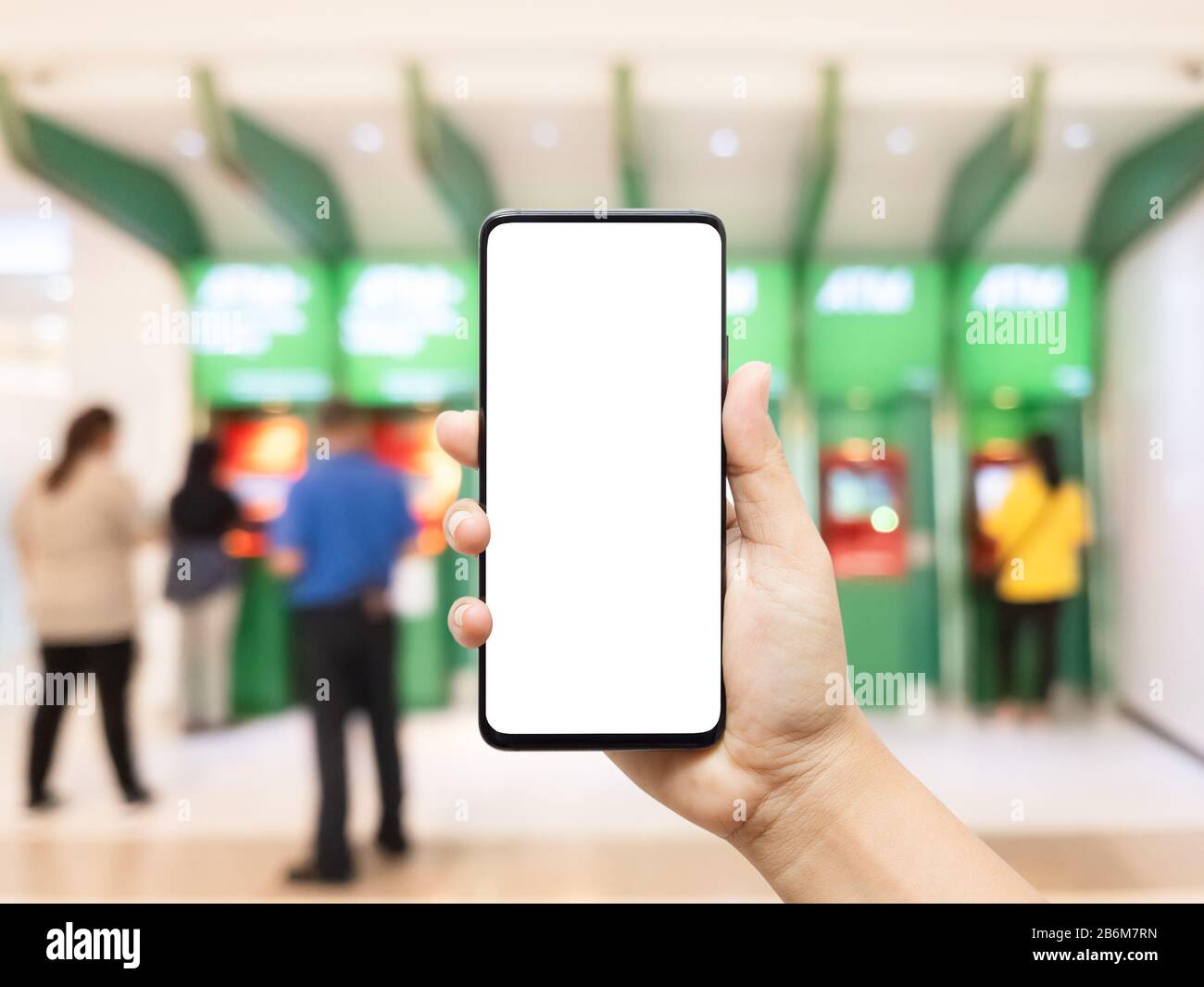 Mockup téléphone portable, main à l'aide d'un smartphone avec un écran vide vide avec image floue des personnes utilisant ATM (machine de Teller automatisée). Services bancaires mobiles, e- Banque D'Images