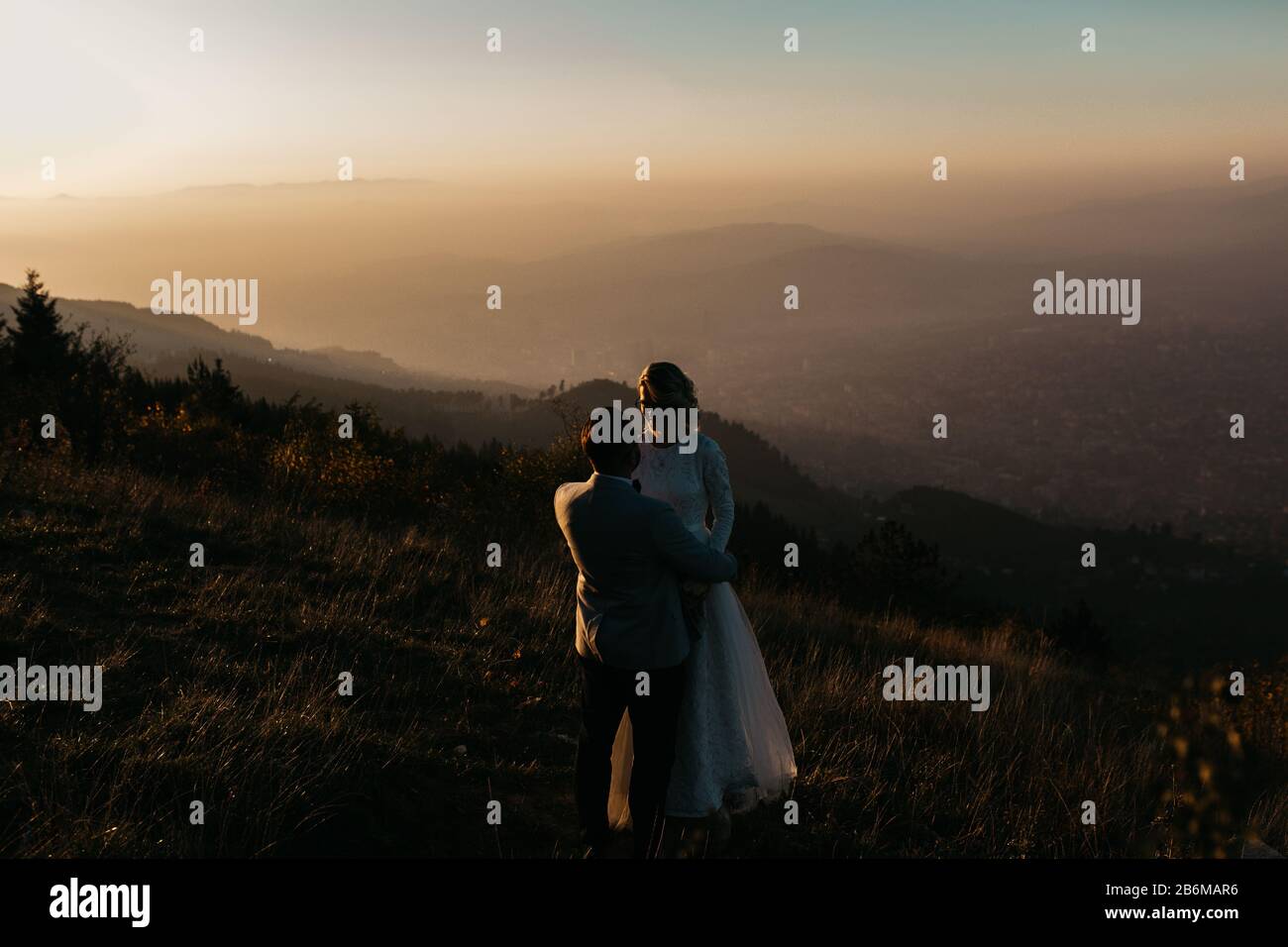 Beau couple ayant un moment romantique sur leur journée de désherbage, dans les montagnes au coucher du soleil. Mariée dans une robe de mariage blanche. Heureux couple embrassant. Banque D'Images