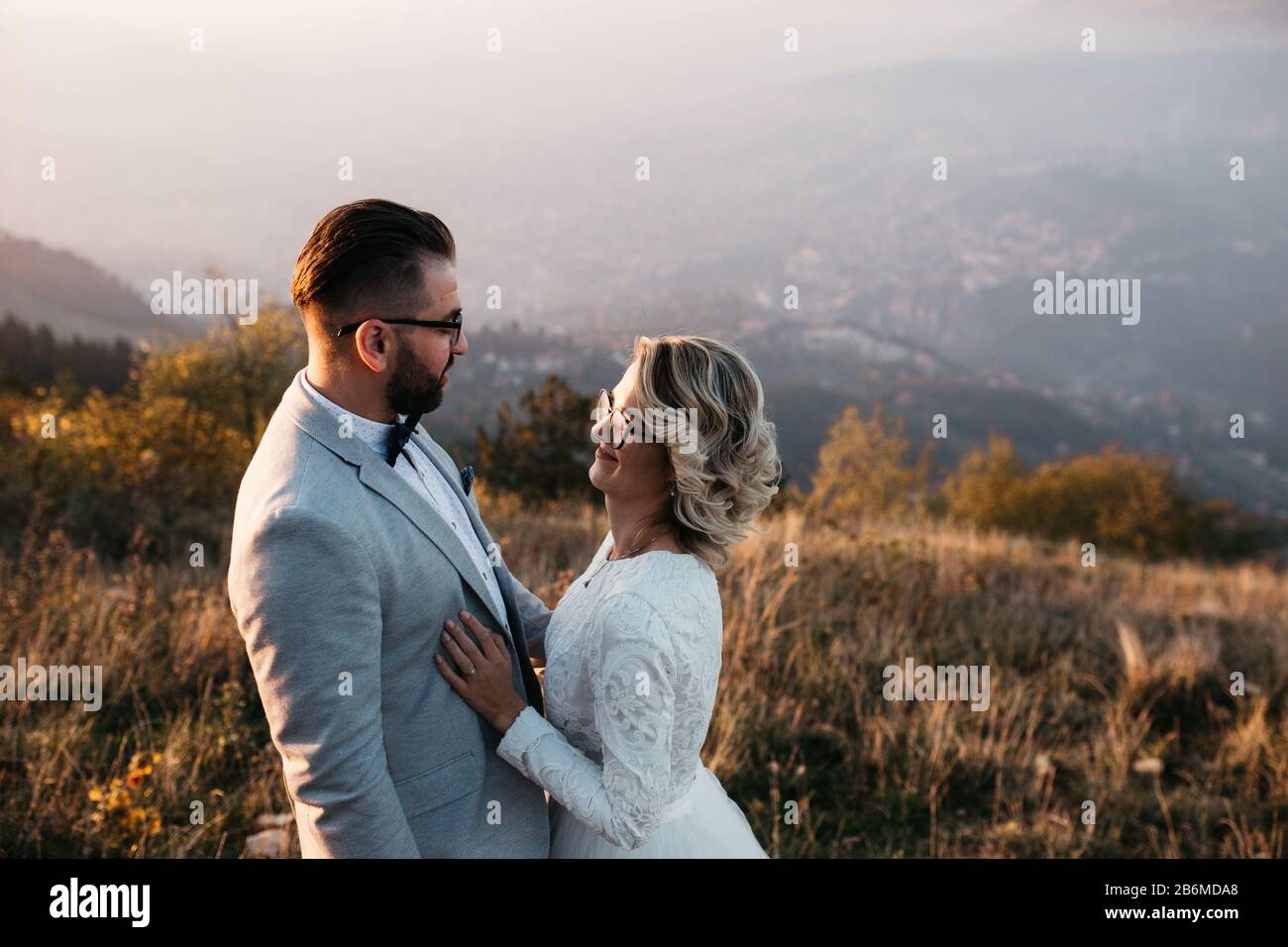 Beau couple ayant un moment romantique sur leur journée de désherbage, dans les montagnes au coucher du soleil. Mariée dans une robe de mariage blanche. Heureux couple embrassant. Banque D'Images