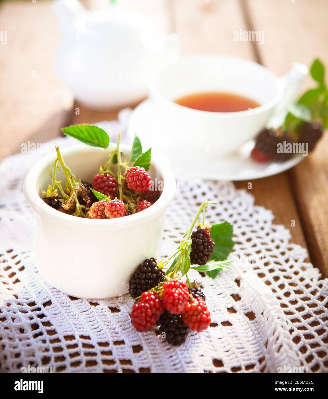 De dessus de framboise fraîche et de mûre avec des feuilles vertes sur table en bois avec un tissu tricoté blanc et une tasse de thé aromatique Banque D'Images