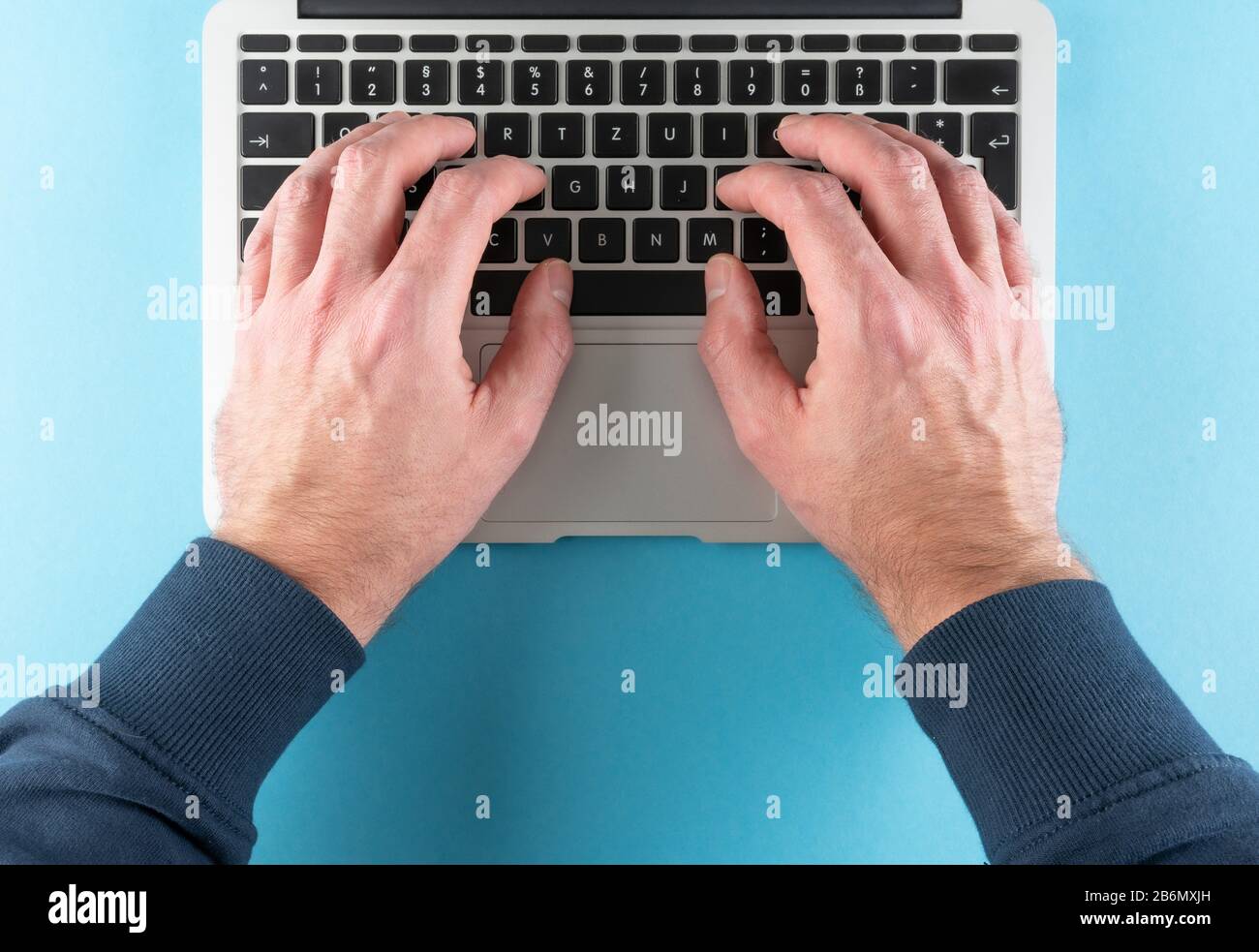 vue de dessus des mains de l'homme dactylographiant sur l'ordinateur portable sur fond bleu de bureau Banque D'Images