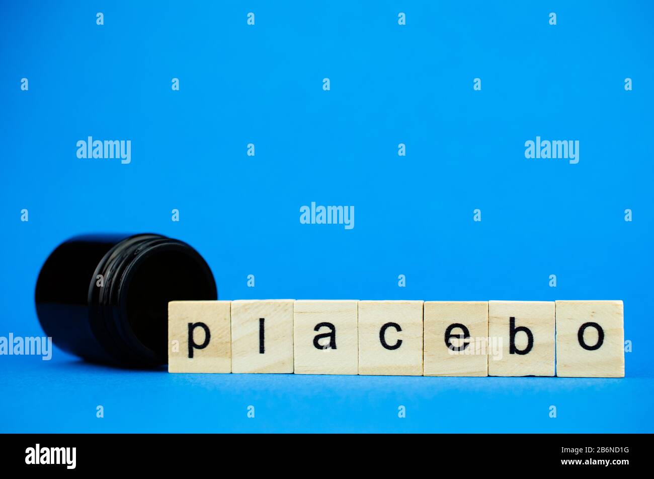 Le mot PLACEBO sur des cubes en bois et une fiole noire médicale sur fond bleu. Banque D'Images