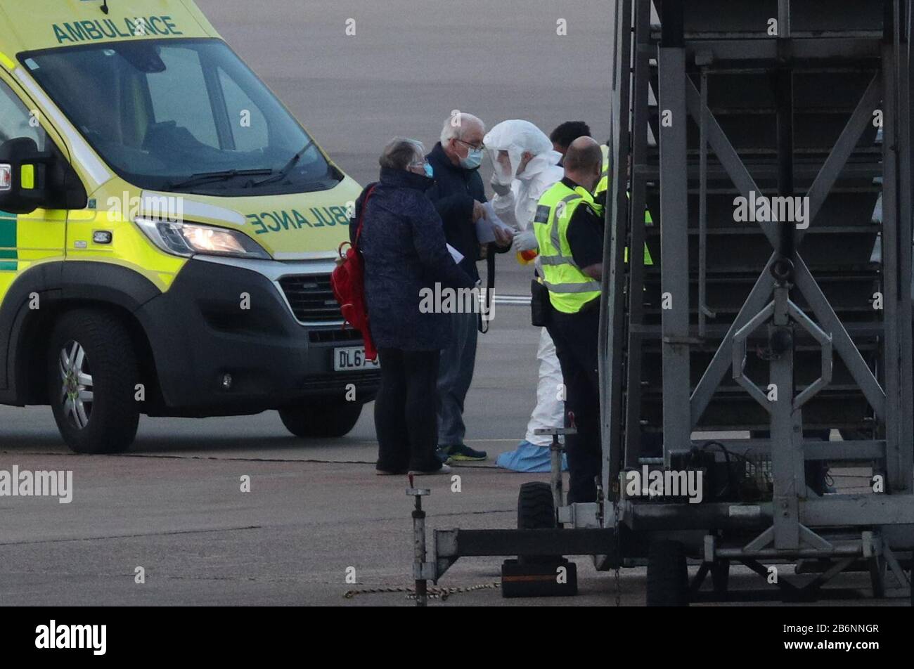 Un membre du NHS West Midlands Ambulance Service, portant des vêtements de protection et un masque facial, parle aux passagers du navire de croisière Grand Princess, qui a été frappé par le coronavirus, après leur rapatriement des États-Unis vers le Royaume-Uni à l'aéroport de Birmingham. Banque D'Images