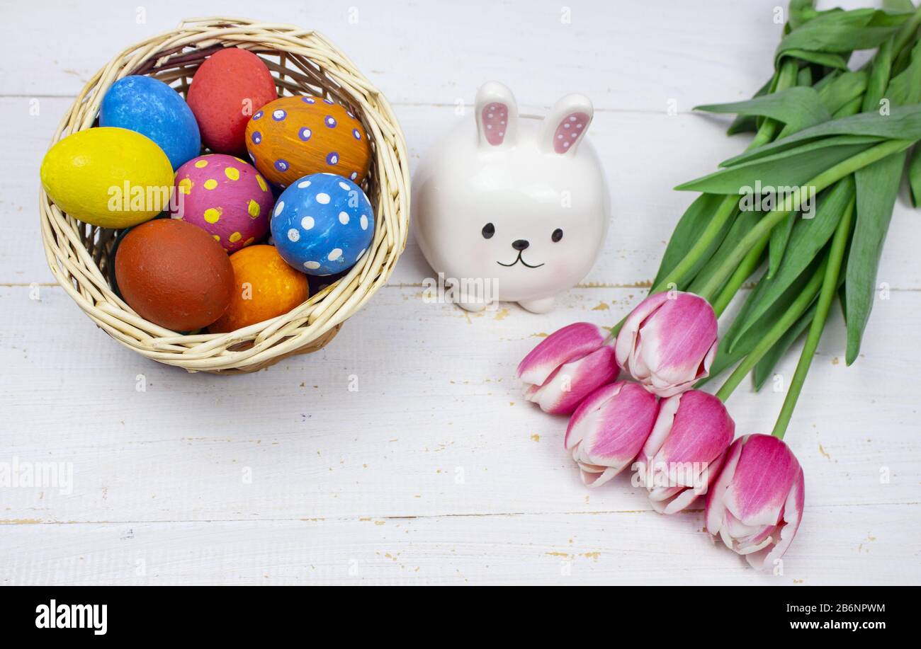 Œufs de Pâques. Oeufs de Pâques multicolores avec tulipes et un lapin sur fond blanc en bois. Œufs dans le panier. Bannière. Tulipes. Espace de copie Banque D'Images