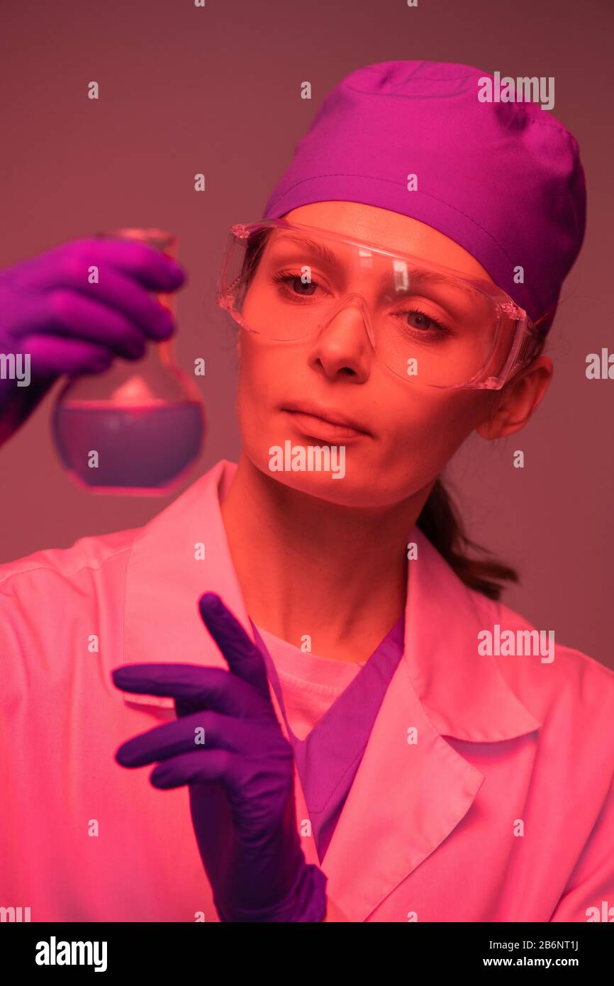 Scientifique féminin dans le CAP et lunettes de sécurité travaillant avec des produits chimiques en laboratoire, effet de lumière rouge Banque D'Images