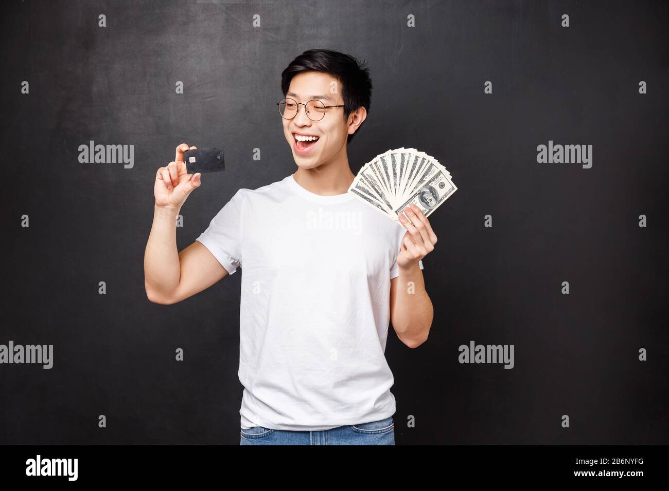 Concept de technologie, d'argent et de prix. Portrait de souriant boastful, le gars asiatique heureux deviennent riches, chanceux de gagner le prix, tenant des dollars et la carte de crédit Banque D'Images