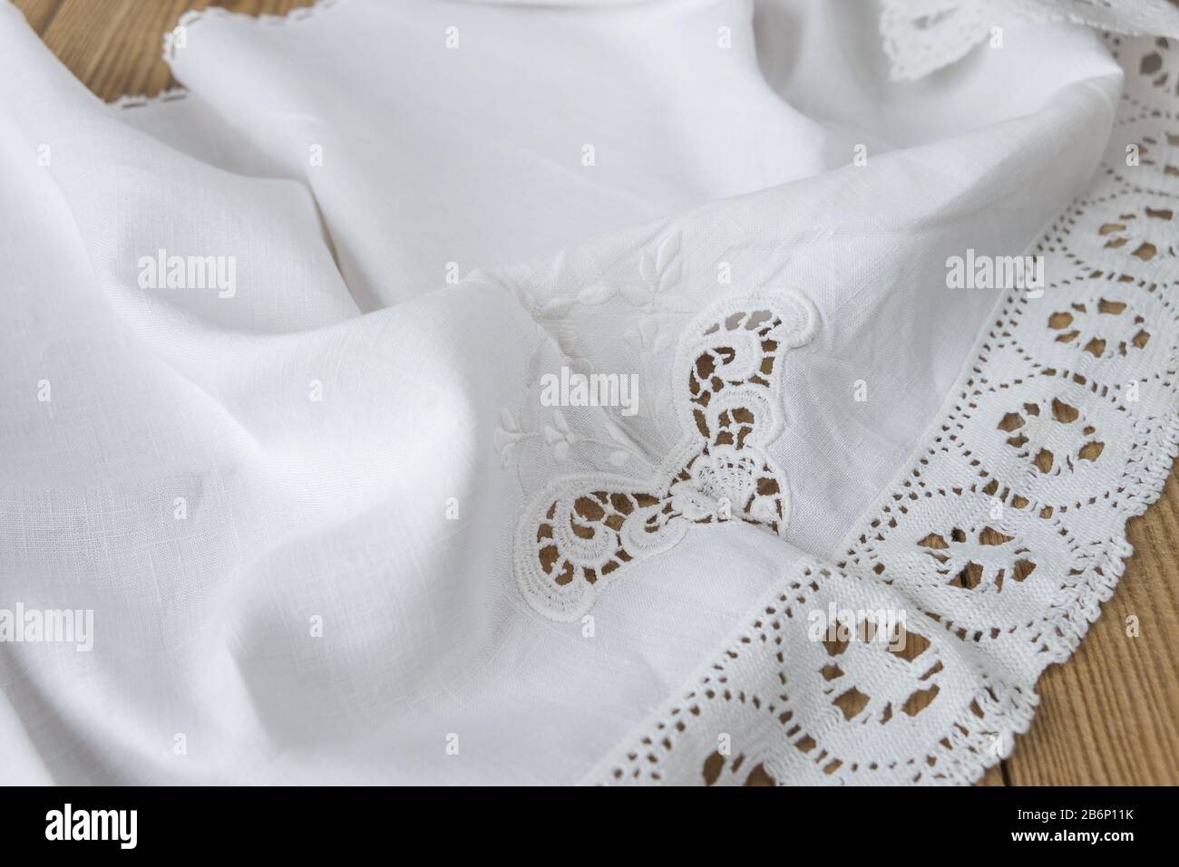 Le tissu blanc en coton naturel avec broderie et dentelle à plis doux se trouve sur une ancienne table en bois Banque D'Images