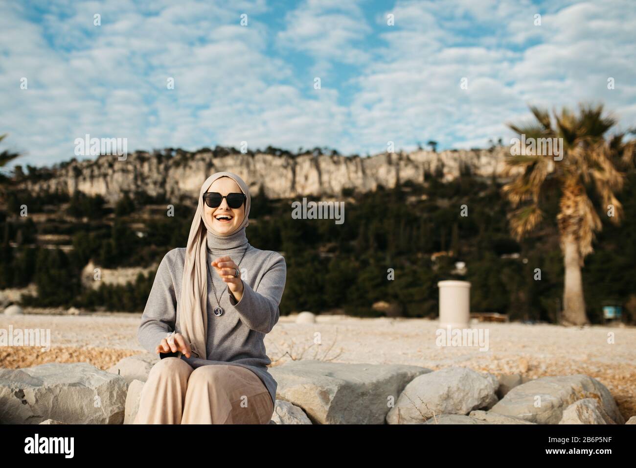 Portrait de jeunes femmes musulmanes européennes avec hijab assis sur la plage en pierre avec la mer en arrière-plan. Il est heureux et détendu. Banque D'Images