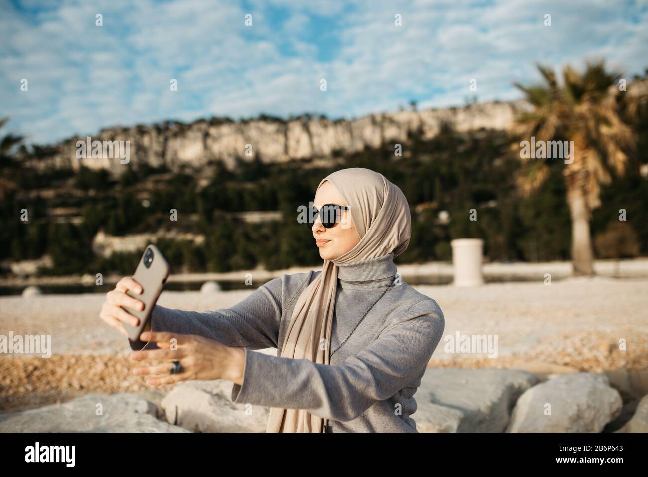 Beau portrait de jeunes femmes musulmanes européennes avec hijab tenant le téléphone mobile et prenant des photos du lac par jour nuageux. Elle envoie des SMS sur Smartph Banque D'Images