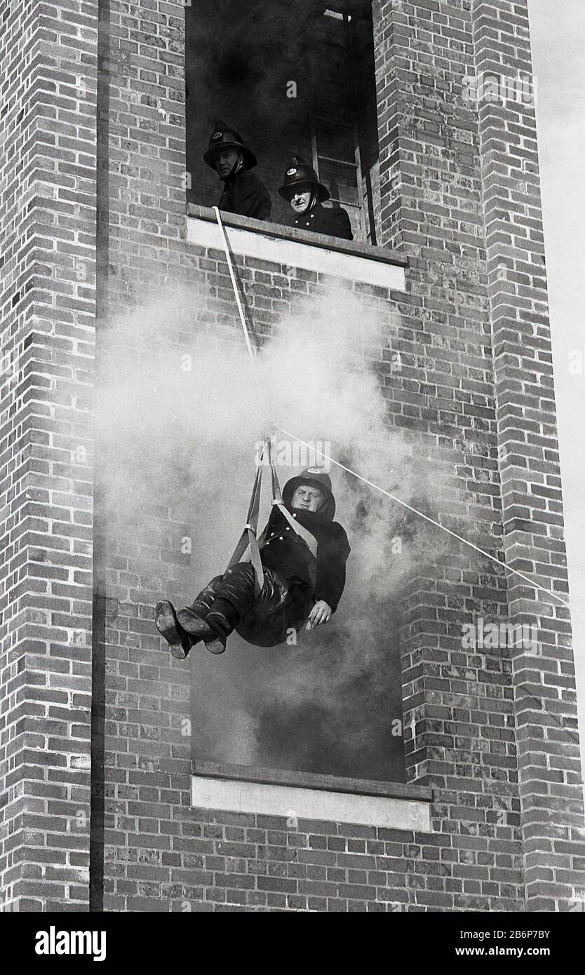 Années 60, historiques, pompiers sur une perceuse d'entraînement, chasseur de feu mâle laissant une tour de briques remplies de fumée sur un harnais de sécurité, Fleetwood, Angleterre, Royaume-Uni Banque D'Images