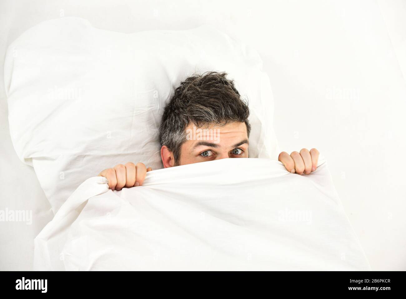 Homme avec se cacher dans le lit sous la couverture à la maison. Guy avec  le visage surpris ou effrayés se pose sous la couverture blanche Photo  Stock - Alamy