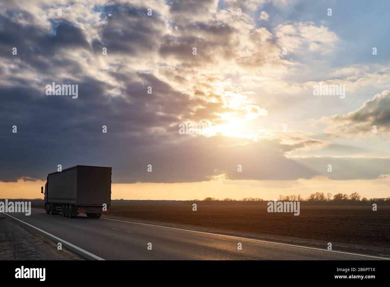 Le camion se déplace sur l'autoroute en toile de fond d'un beau nuage au coucher du soleil. Banque D'Images