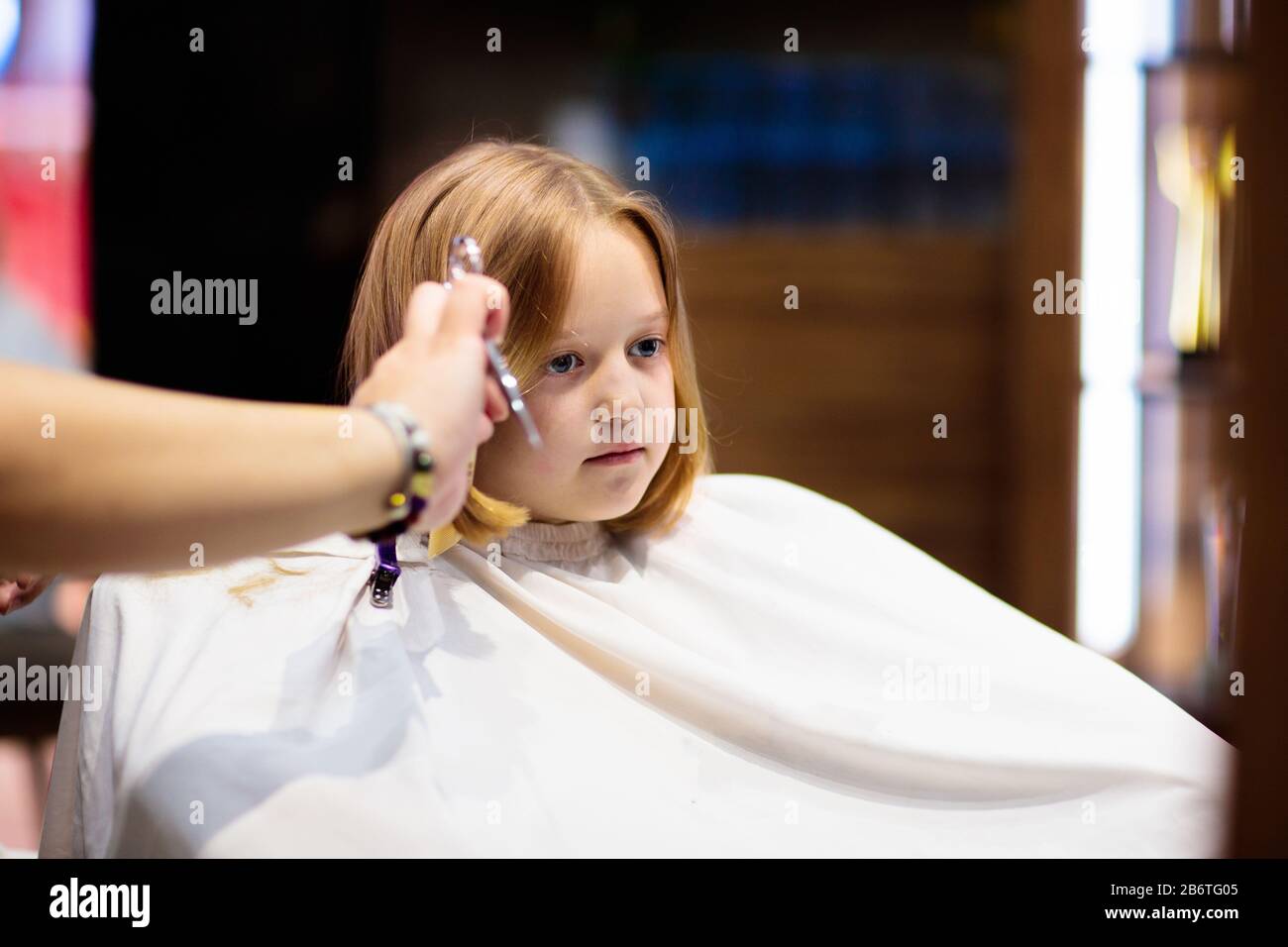 Enfant en train de se délailler dans le salon de beauté. Coiffeur coupe les cheveux. Petite fille avec Bob blond foncé à l'épaule chez styliste. Spa pour enfants. Style et fashi Banque D'Images