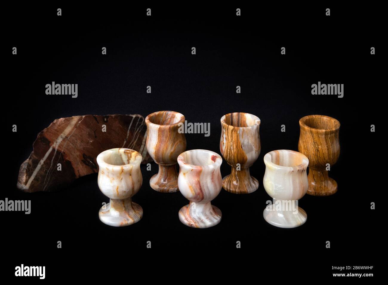 Ensemble de six verres en pierre d'onyx naturel et gros morceau de jasper isolé sur fond sombre Banque D'Images