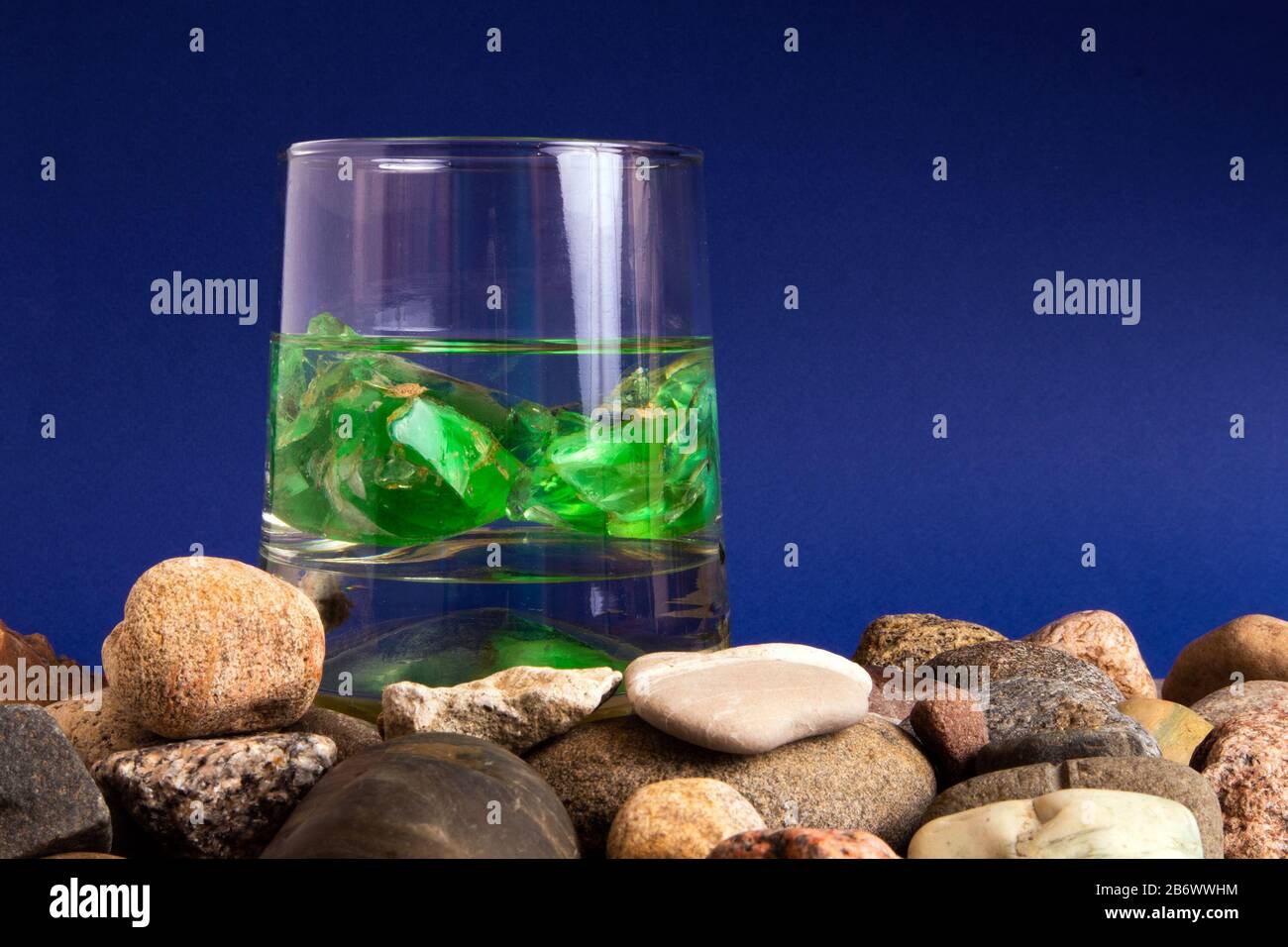 Verre avec de l'eau et deux pierres gemmes vertes à l'intérieur debout sur une pile de galets Banque D'Images