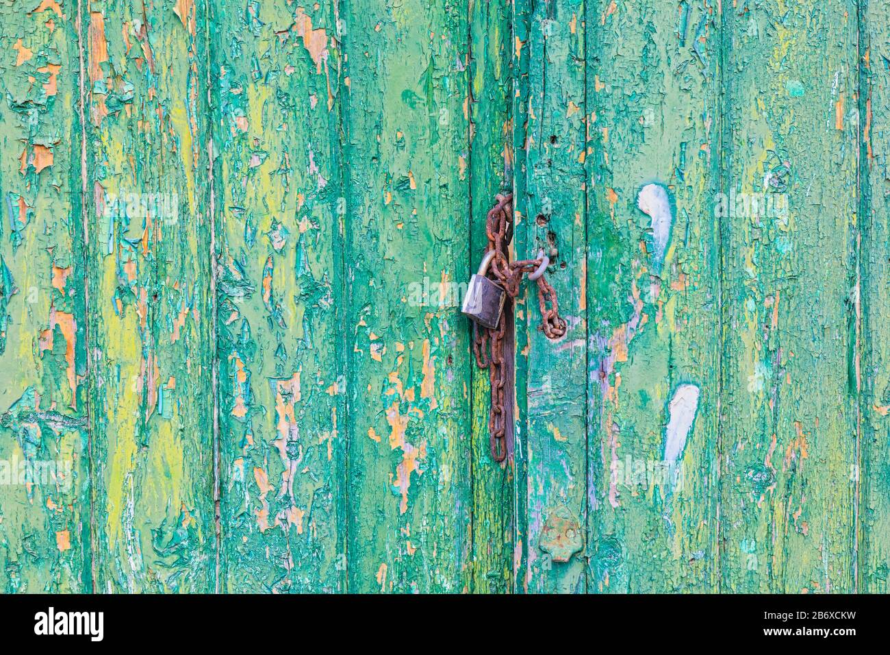 Serrure rouillée et chaîne tenant les portes cousues avec peinture jaune et verte écaillée fermée. Banque D'Images