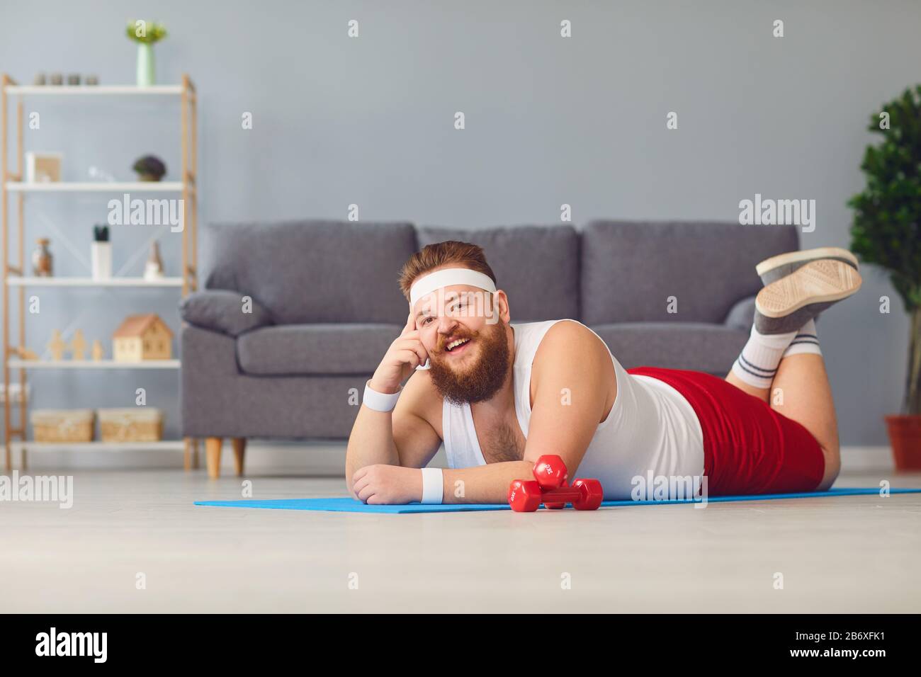 Drôle de graisse rouge homme faisant des exercices sur le sol souriant tout en couché sur le sol à la maison. Banque D'Images