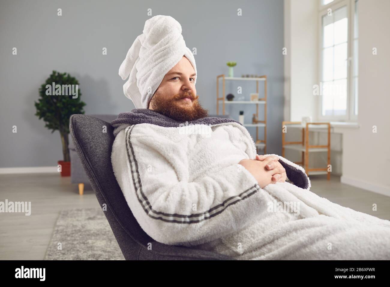 Un homme étrange et drôle barbu dans un peignoir fait des soins au spa sur son visage repose dans une chambre Banque D'Images